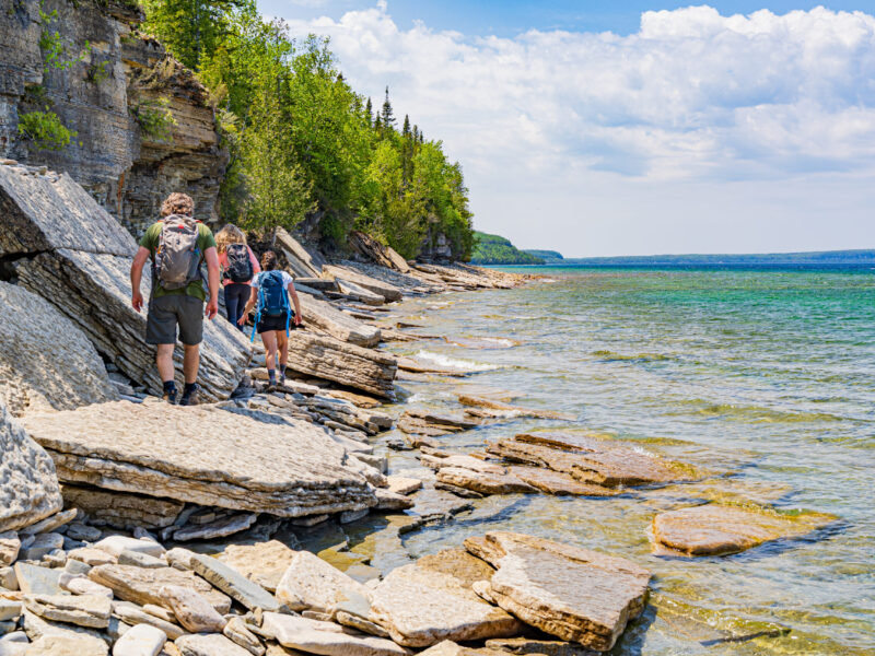 Hero image of group hiking north along the Georgian Bay shoreline of the Bruce Peninsula with Lions head in the distance.